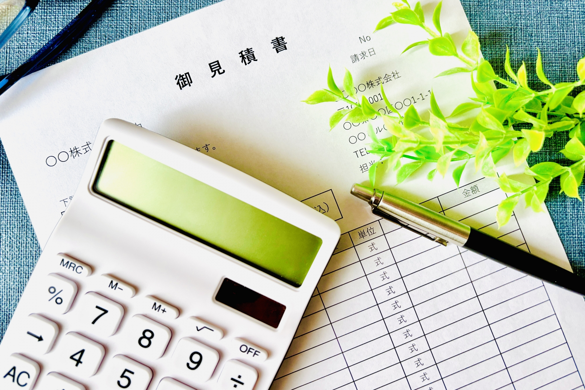 御見積書と電卓、ペン、観葉植物が並べられたデスク上の様子