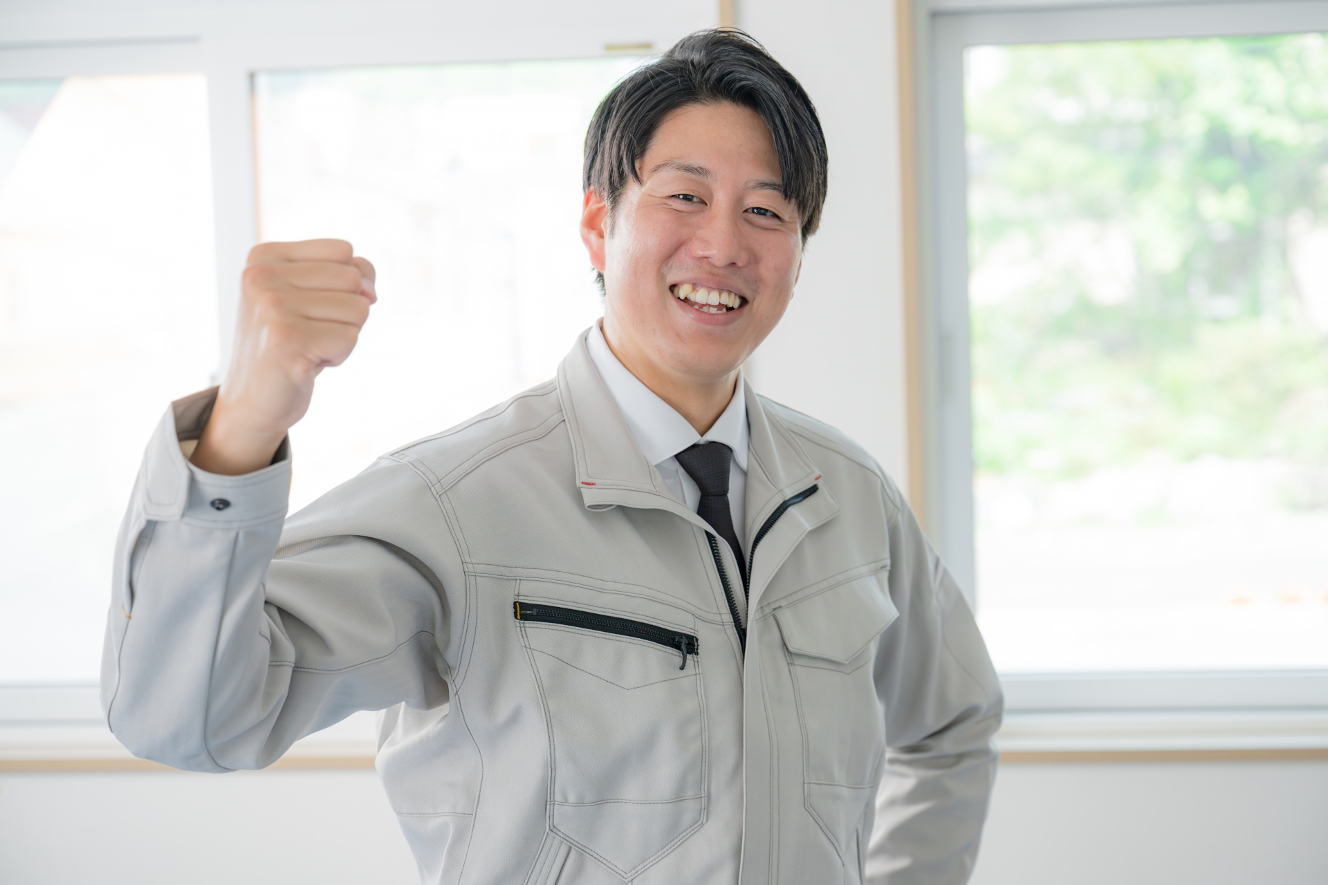 笑顔でガッツポーズをする作業服姿の男性スタッフ。給湯器交換の専門業者として、お客様に安心と信頼を届ける様子を表しています。
