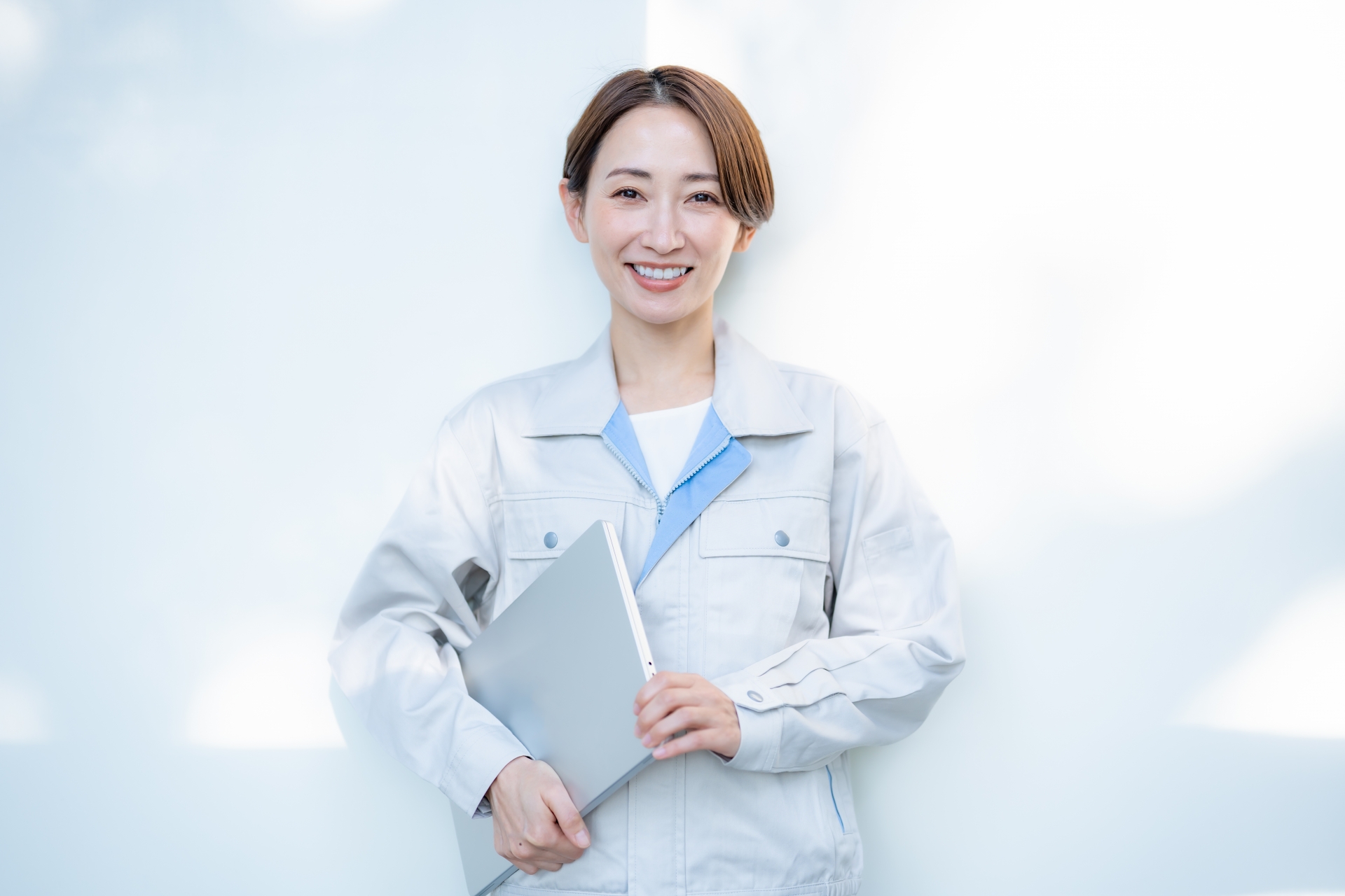 作業服姿の女性スタッフがノートパソコンを手にしながら笑顔で立っている様子。給湯器交換の業務を安心して任せられる専門スタッフを表現しています。