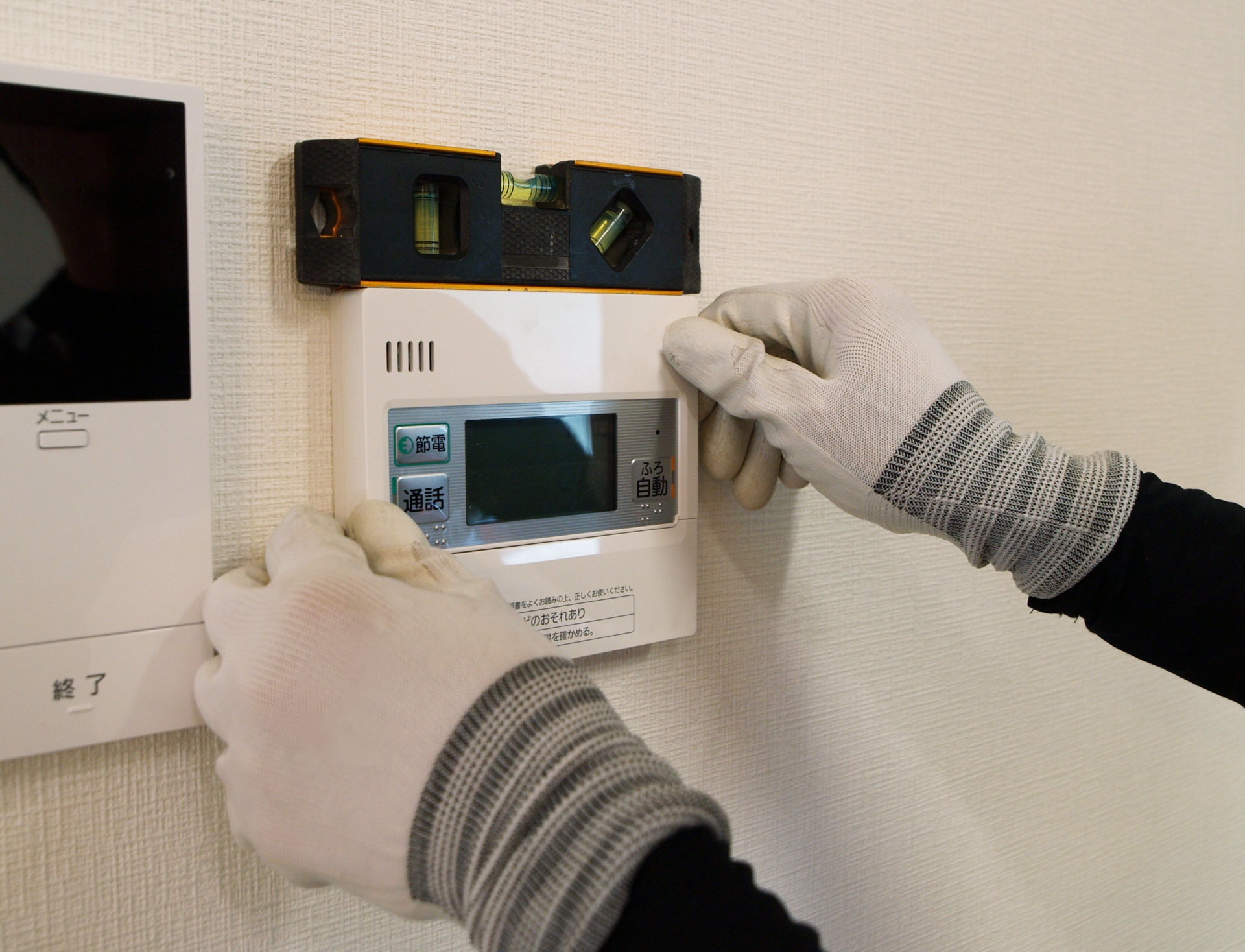 ヘルメットを着用した作業員が屋外で給湯器交換工事を行っている様子。壁面の配管や機器を点検しながら丁寧に施工している場面です。